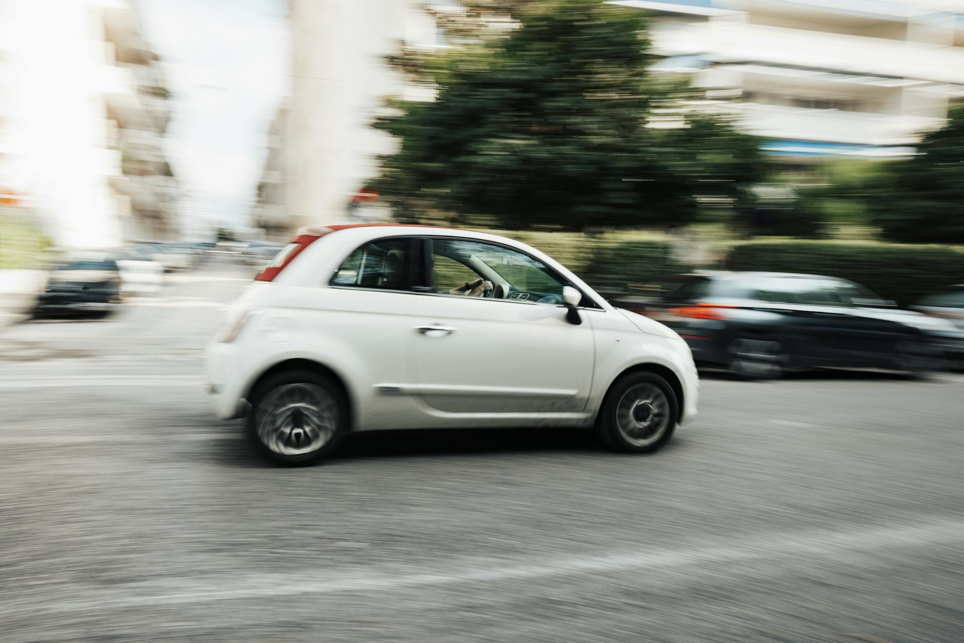 Białe auto jedzie szybko po ulicy w Zamościu, rozmyte tło miasta