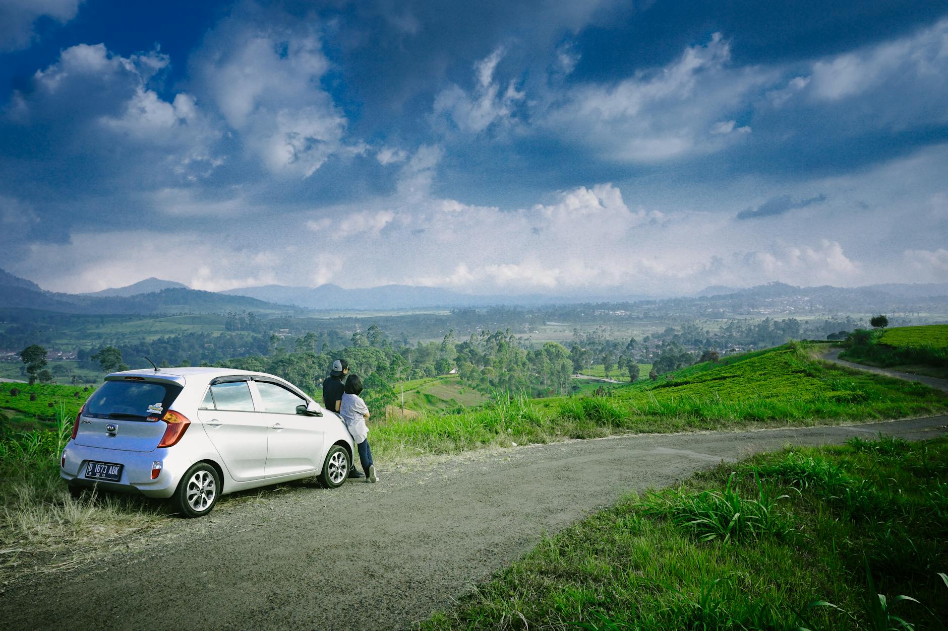 Para przy samochodzie patrzy na zielone pola i góry w pochmurny dzień